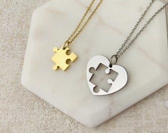 May include: Two necklaces with matching puzzle piece pendants. One necklace has a gold-toned puzzle piece pendant, and the other has a silver-toned heart pendant with a puzzle piece cutout.