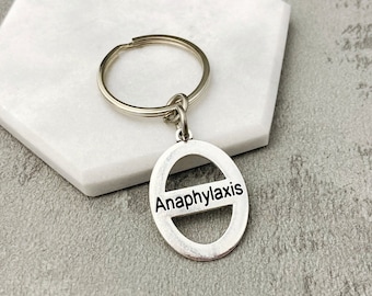 May include: Silver keyring with a round tag that says "Anaphylaxis" in black lettering. The tag has a horizontal line through the centre.