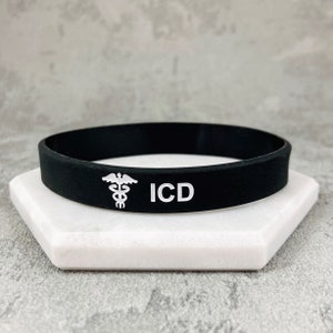 Może przedstawiać: Czarna silikonowa bransoletka z białym symbolem medycznym i nadrukiem "ICD".