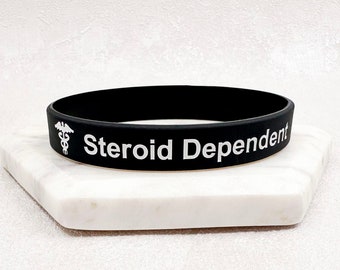 May include: Black silicone bracelet with white text that reads "Steroid Dependent" and a caduceus symbol.