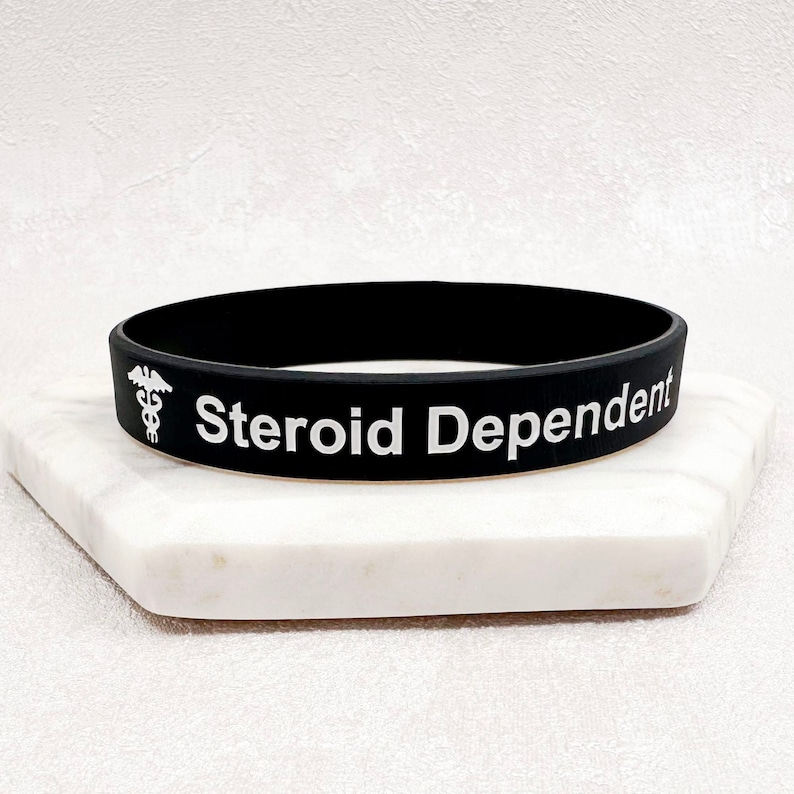 Peut inclure: Bracelet en silicone noir avec le texte blanc "Steroid Dependent" et un symbole de caduc&eacute;e.