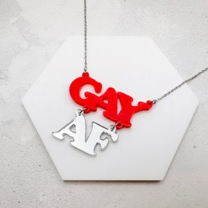 Peut inclure: Un collier en chaîne argent avec un pendentif en acrylique rouge qui dit "GAY AF".