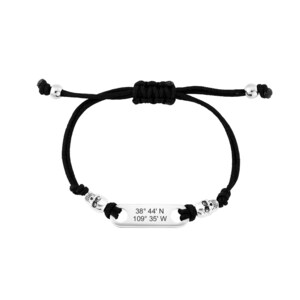 May include: Black cord bracelet with silver skull beads and a silver rectangular tag engraved with the coordinates "38° 44' N 109° 35' W".
