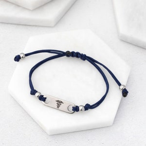 May include: A blue adjustable bracelet with a silver medical symbol charm. The charm is rectangular and has a raised medical symbol.