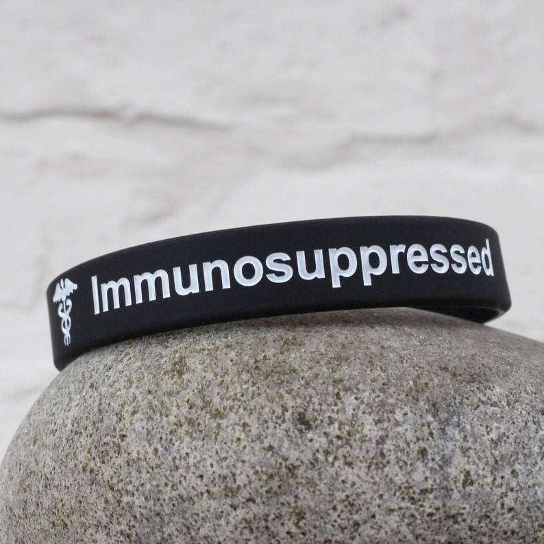 Puede incluir: Pulsera de silicona negra con el texto "Inmunodeprimido" y un s&iacute;mbolo m&eacute;dico blanco.