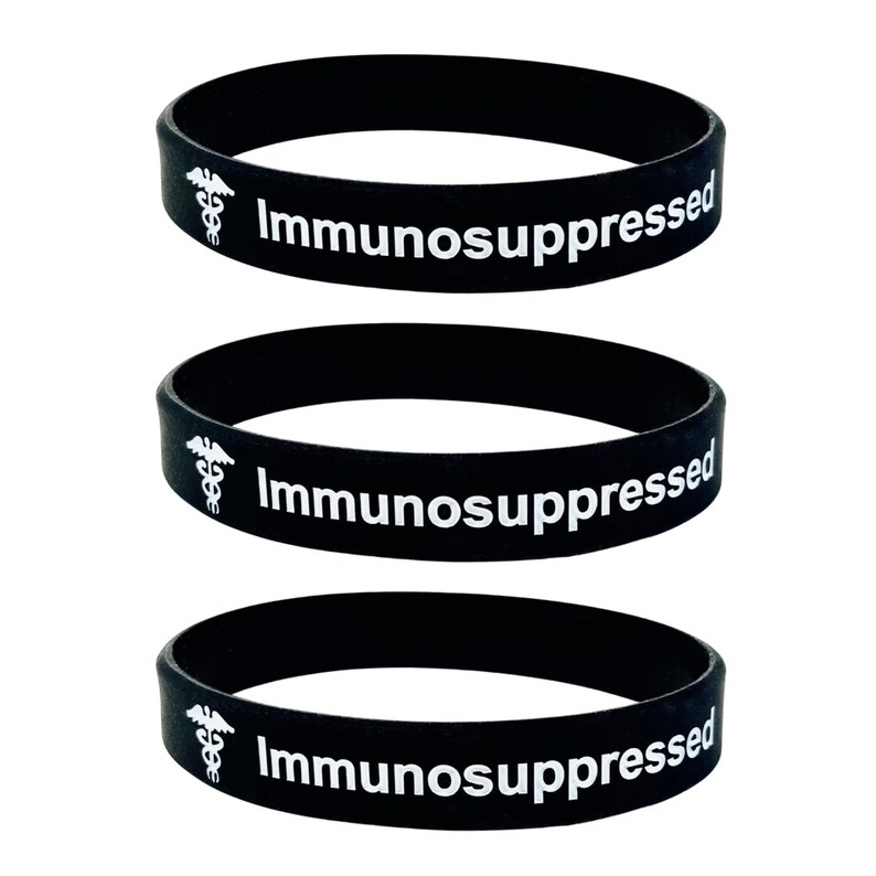 Puede incluir: Tres pulseras de silicona negras con el texto "Inmunodeprimido" y un s&iacute;mbolo m&eacute;dico blanco.