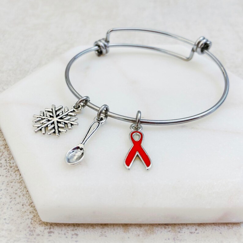 May include: A silver bangle bracelet with three charms: a snowflake, a spoon, and a red awareness ribbon.