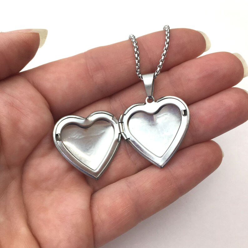 May include: A silver heart-shaped locket necklace, open to reveal the interior. The locket hangs from a delicate chain. The locket is held open, showcasing its reflective surfaces. A classic piece of jewelry.