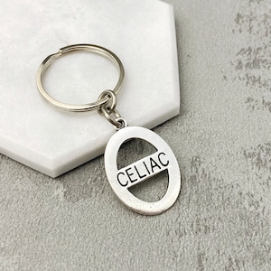 May include: Silver keyring with a round tag that says "CELIAC" in all caps. The tag has a line through the centre.