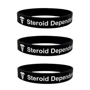 Peut inclure: Trois bracelets en silicone noir avec le texte "Steroid Dependent" et un symbole de caduc&eacute;e blanc.