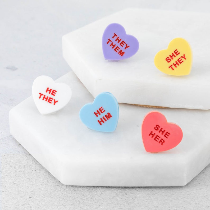 Set of LGBTQ+ pronoun pins showing all available designs and colour variations laid out together