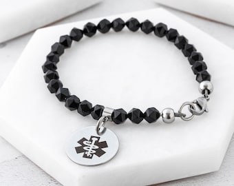 Puede incluir: Pulsera de cuentas negras con un dije de acero inoxidable con un símbolo médico. La pulsera tiene un cierre de langosta.