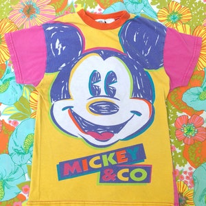 May include: Yellow t-shirt featuring a colourful Mickey Mouse graphic and the text "Mickey & Co."