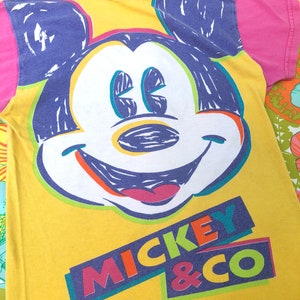 May include: Yellow t-shirt featuring a colourful Mickey Mouse graphic and the text "Mickey & Co."