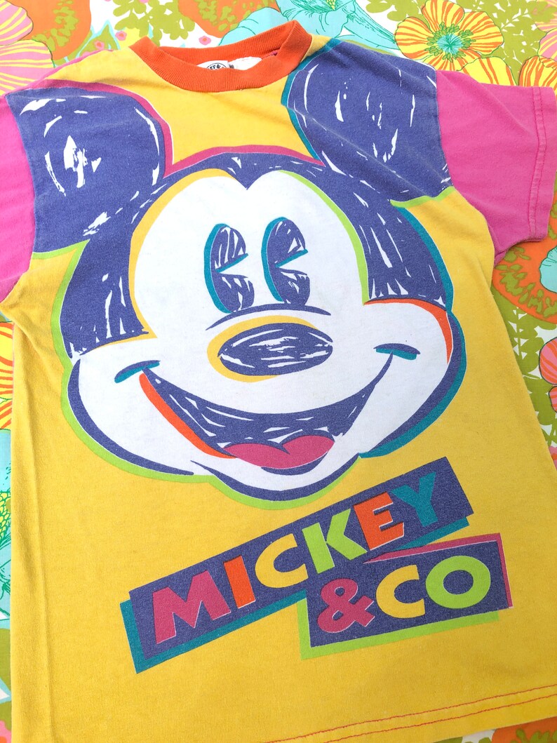 May include: Yellow t-shirt featuring a colourful Mickey Mouse graphic and the text "Mickey & Co."
