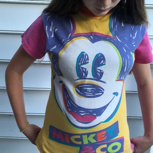 May include: A yellow t-shirt featuring a colourful Mickey Mouse graphic and the text "Mickey & Co."