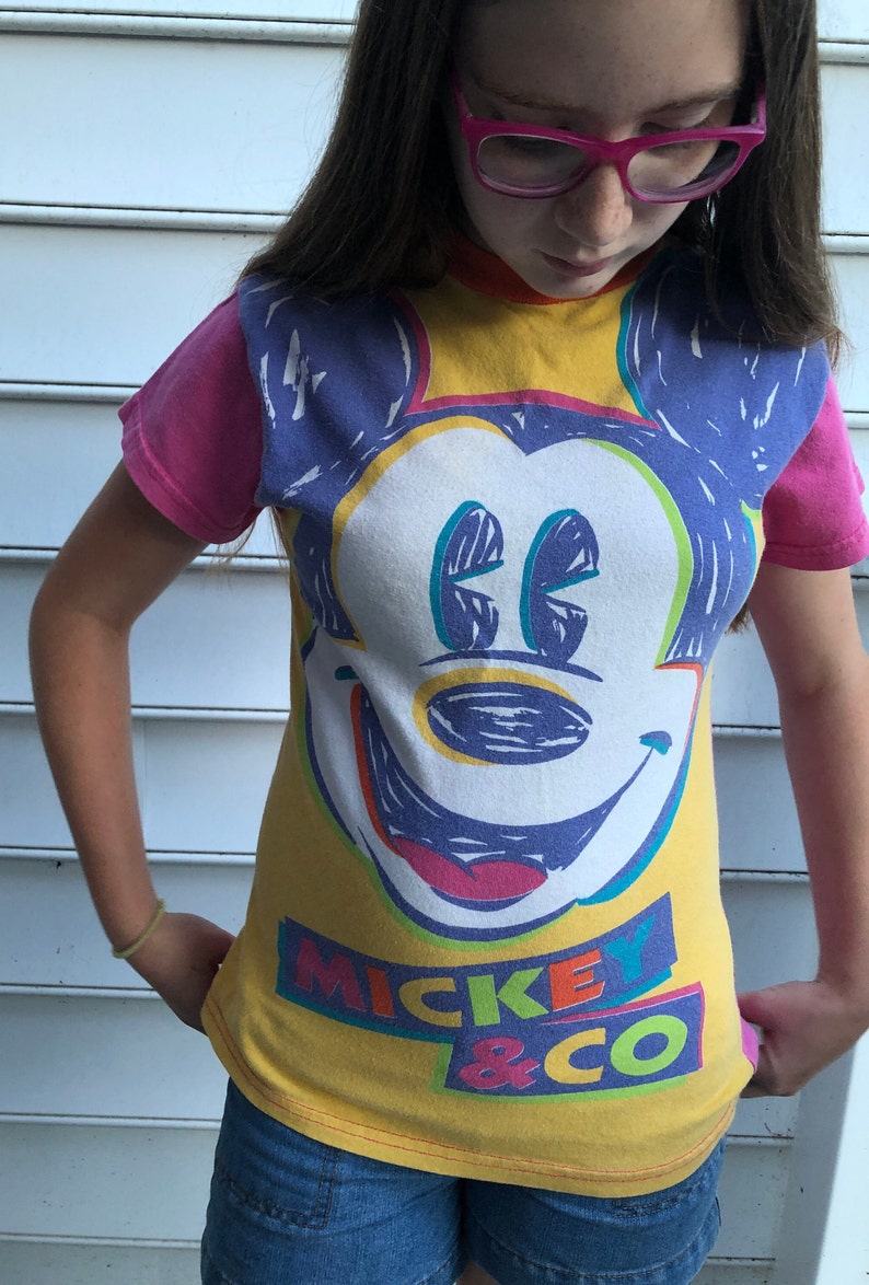 May include: A yellow t-shirt featuring a colourful Mickey Mouse graphic and the text "Mickey & Co."