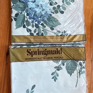 Könnte beinhalten: Zwei Packungen Springmaid Wondercale bügelfreie Perkal-Bettwäsche für ein Doppelbett. Die Bettwäsche hat ein Blumenmuster mit blauen Blüten und grünen Blättern auf weißem Hintergrund. Die Verpackung enthält den Markennamen, die Produktbeschreibung und die Stoffzusammensetzung: 65 % Kodel-Polyester und 35 % Baumwolle.