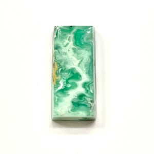 May include: A green and white cabochon gemstone with a swirling pattern. The gemstone is rectangular in shape and has a polished finish.
