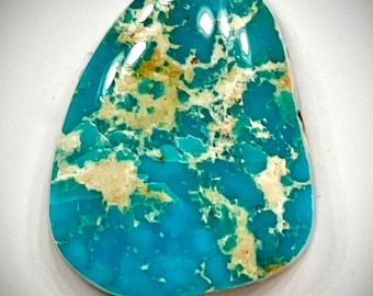 May include: A turquoise cabochon with a blue-green color and white and brown matrix. The stone is oval shaped and has a smooth, polished surface.