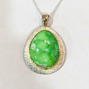 May include: A green gemstone pendant with a silver and gold setting. The pendant is on a silver chain.