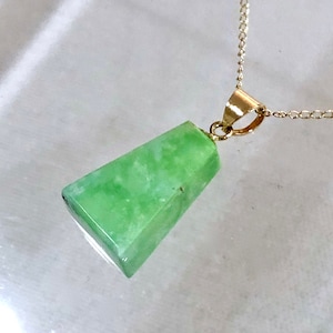 May include: A gold chain necklace with a green gemstone pendant. The pendant is a triangular shape with a smooth, polished surface.