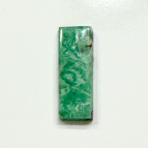 May include: A green and white cabochon gemstone with a swirling pattern. The gemstone is rectangular in shape and has a smooth, polished surface.