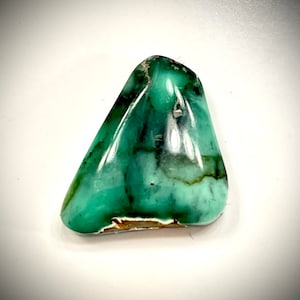 May include: A green, translucent, irregularly shaped gemstone with brown veins.