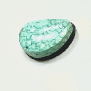 May include: A turquoise cabochon gemstone with a black backing. The stone has a unique, patterned surface.