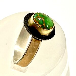 May include: A silver and gold ring with a green turquoise stone set in a black bezel.