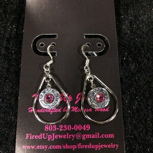 May include: A pair of silver dangle earrings with pink rhinestones set in a bullet casing. The earrings are on a black background with the text "FiredUpJewelry@gmail.com" and "www.etsy.com/shop/firedUpjewelry".