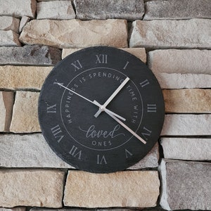 Puede incluir: Reloj redondo negro con números romanos y el texto "Happiness is spending time with loved ones".