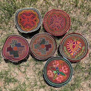 Pode incluir: Seis bases para copos redondas, costuradas à mão, com intrincados desenhos geométricos e florais coloridos. As bases para copos apresentam uma variedade de padrões em tons de vermelho, castanho, verde, azul e laranja, com costuras detalhadas nas bordas.