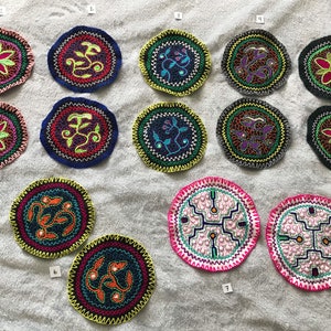 Pode incluir: Doze  copos de tecido bordado redondos com vários desenhos coloridos. Os desenhos incluem flores, folhas e padrões geométricos. Os copos têm aproximadamente 10 cm de diâmetro.