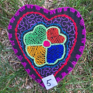 May include: A purple heart-shaped fabric patch with a colorful embroidered flower design in the center. The flower has four petals in shades of green, red, yellow, and blue. The patch has a white tag with the number "5" on it.