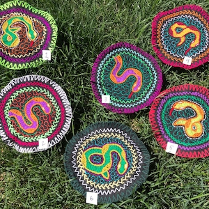 Pode incluir: Seis patches redondos bordados coloridos com um design de cobra. Cada patch tem um esquema de cores diferente e um número de 1 a 6 no canto inferior direito.