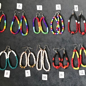 May include: Thirteen pairs of beaded earrings, each with a unique color combination. The earrings are oval-shaped and feature a variety of colors, including red, blue, green, yellow, black, and white. The earrings are numbered 1 through 13.