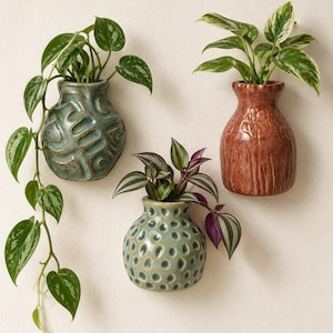 May include: Three ceramic wall-mounted vases in blue-green and reddish-brown tones. The top left vase has a textured geometric pattern, the bottom center vase features a dimpled surface, and the right vase displays a floral relief design.