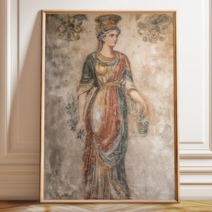 Puede incluir: Impresión enmarcada de un fresco clásico que representa a una mujer con túnicas drapeadas, sosteniendo una ramita y un jarrón. La obra de arte presenta una paleta de colores apagados de rojos, verdes y dorados, sobre un fondo texturizado y envejecido. El marco es marrón claro y cálido.