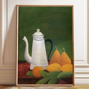 Puede incluir: Un óleo enmarcado que representa una cafetera blanca con asa negra junto a dos peras amarillas y una naranja sobre una superficie de color rojo oscuro. El fondo es de un verde oscuro sólido, creando un bodegón con frutas.