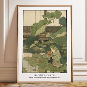 Puede incluir: Lámina artística enmarcada que representa una rana con una túnica verde, sosteniendo una taza, entre nenúfares y grandes hojas verdes. La obra tiene una estética japonesa, con el texto: "Quiet moments are what nurture the soul."