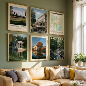 May include: A gallery wall featuring six framed posters of Saratoga Springs, New York. The prints display the racetrack, the Adelphi Hotel, a city map, Congress Park, a pavilion reflecting in water, and Geyser Creek, all in light wood frames.