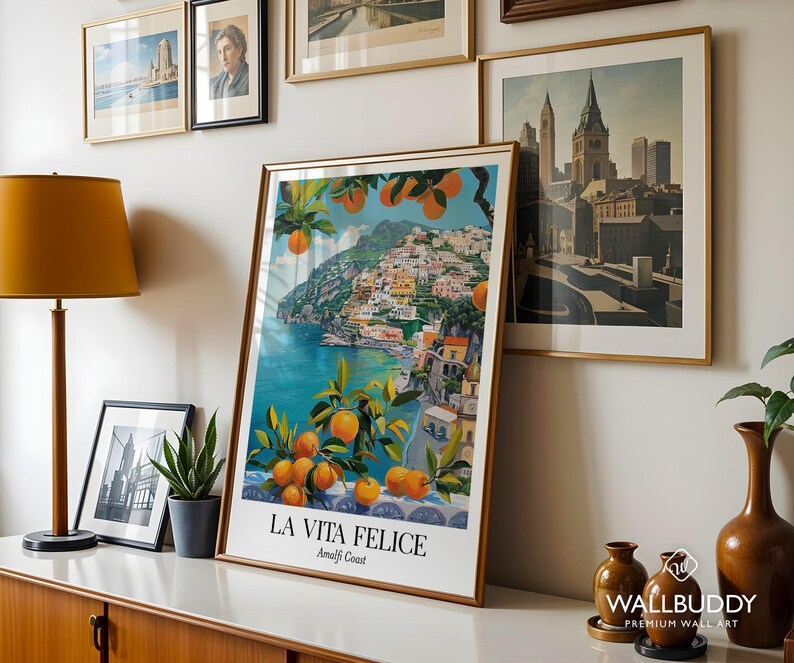 Peut inclure: Une impression d'art verticale encadr&eacute;e intitul&eacute;e LA VITA FELICE Amalfi Coast, pr&eacute;sentant une illustration vibrante de la c&ocirc;te italienne avec une eau turquoise, des b&acirc;timents color&eacute;s &agrave; flanc de colline et des branches charg&eacute;es d'agrumes orange.