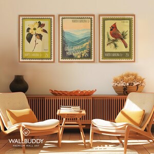 Może przedstawiać: Trzy oprawione wydruki w stylu vintage z wizerunkami Karoliny P&oacute;łnocnej. Jeden wydruk przedstawia kwiat derenia, drugi Great Smoky Mountains, a trzeci czerwonego kardynała. Każdy wydruk zawiera napis "North Carolina" i cenę 25&cent;.