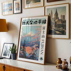 May include: A framed vertical poster featuring a stylised illustration of Mount Fuji with pink cherry blossoms, pine trees, and a reflective lake. The text reads 壮大な地平線, 富士山, and FUJISAN. The poster is displayed in a gold frame.