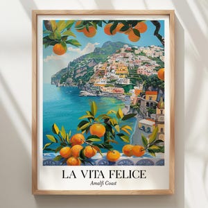 Peut inclure: Une impression d'art encadr&eacute;e repr&eacute;sentant une ville c&ocirc;ti&egrave;re sur une falaise surplombant une mer bleue, encadr&eacute;e par des branches d'oranger avec des fruits orange vif. Le texte LA VITA FELICE Amalfi Coast est imprim&eacute; en noir en bas.