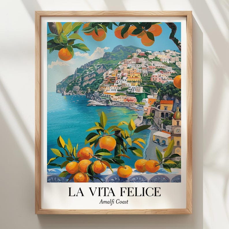 Peut inclure: Une impression d'art encadr&eacute;e repr&eacute;sentant une ville c&ocirc;ti&egrave;re sur une falaise surplombant une mer bleue, encadr&eacute;e par des branches d'oranger avec des fruits orange vif. Le texte LA VITA FELICE Amalfi Coast est imprim&eacute; en noir en bas.
