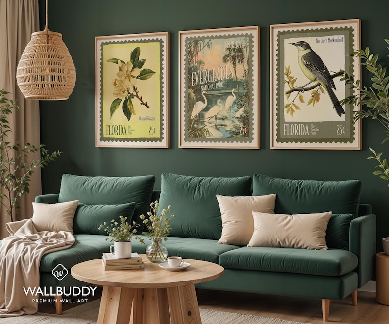 May include: Three framed vintage-style prints depicting Florida scenes. The prints feature a magnolia flower, Everglades National Park with herons, and a Northern Mockingbird. The prints are displayed above a green velvet sofa with beige cushions.