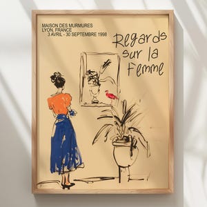 Op de afbeelding: Een ingelijste poster met een gele achtergrond en zwarte lijntekeningen van een vrouw in een blauwe rok en oranje top, een plant in een pot en een rode vogel. De tekst op de poster luidt "MAISON DES MURMURES LYON, FRANKRIJK 3 APRIL - 30 SEPTEMBER 1998 Regards sur la Femme".