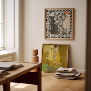 May include: Two square framed art prints. The top print features two figures in black and white with geometric patterns. The bottom print displays a golden, yellow-toned painting of two figures embracing amidst a field of colourful floral patterns.